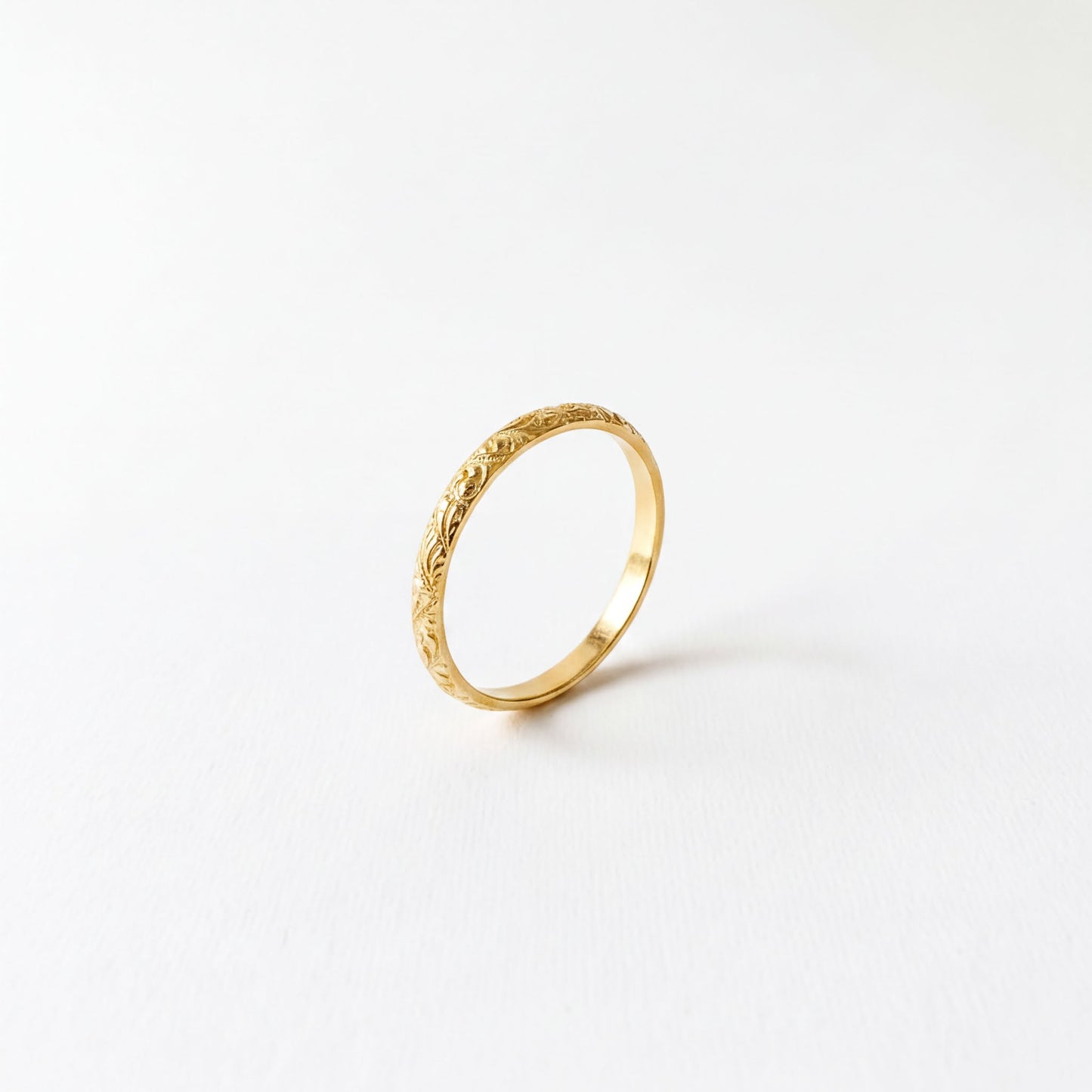 A single gold ring with an intricate floral design on the band is shown against a plain white background.