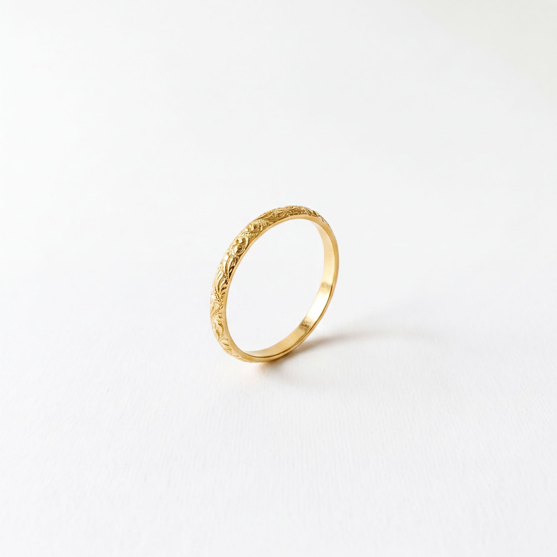 A single gold ring with an intricate floral design on the band is shown against a plain white background.